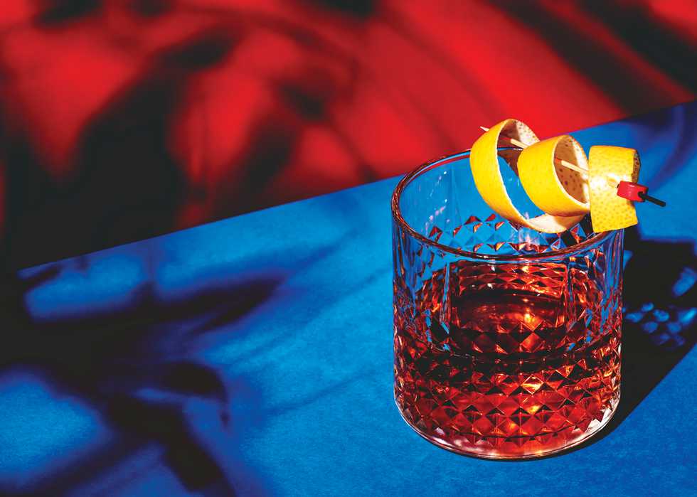 Sazerac, classic alcoholic cocktail with cognac, bourbon, absinthe, bitters, sugar and lemon zest. Dazzling red blue background with hard light and harsh shadows